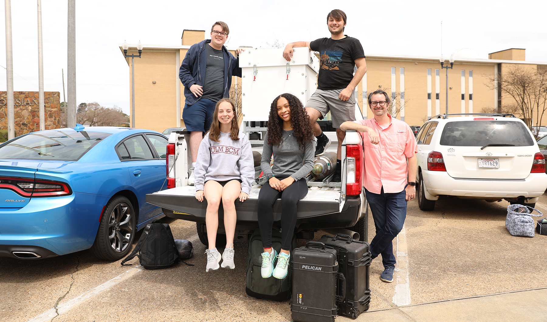 Four students and their professor sit and stand around the ULM storm chaser truck.