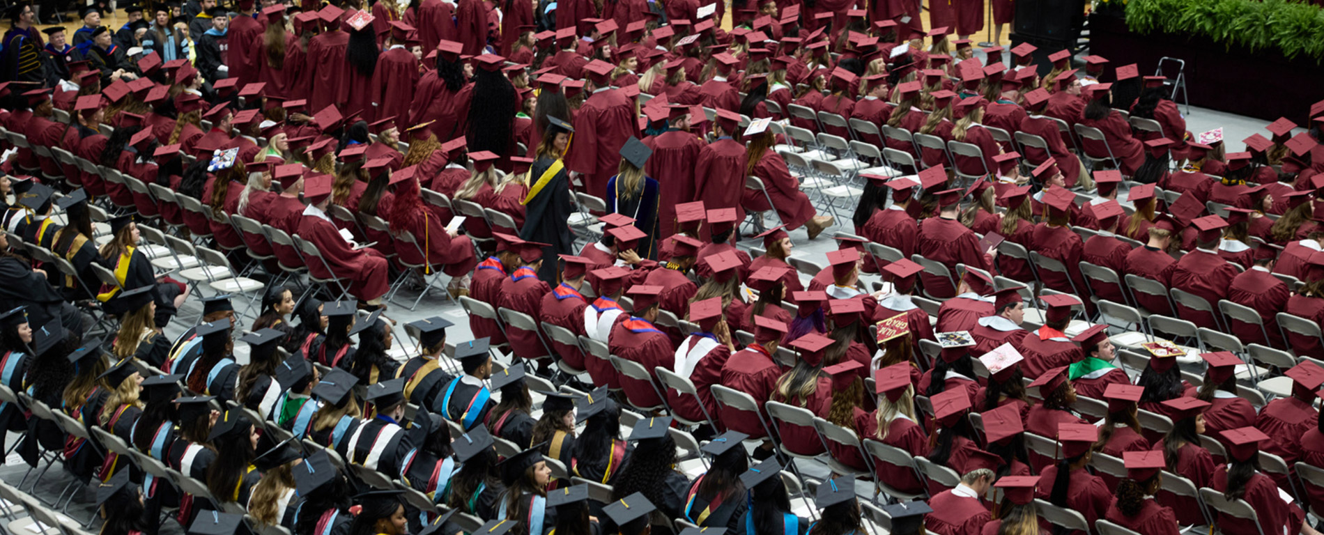 students dressed in cap and gown, seated in coliseum, preparing to graduate during commencement