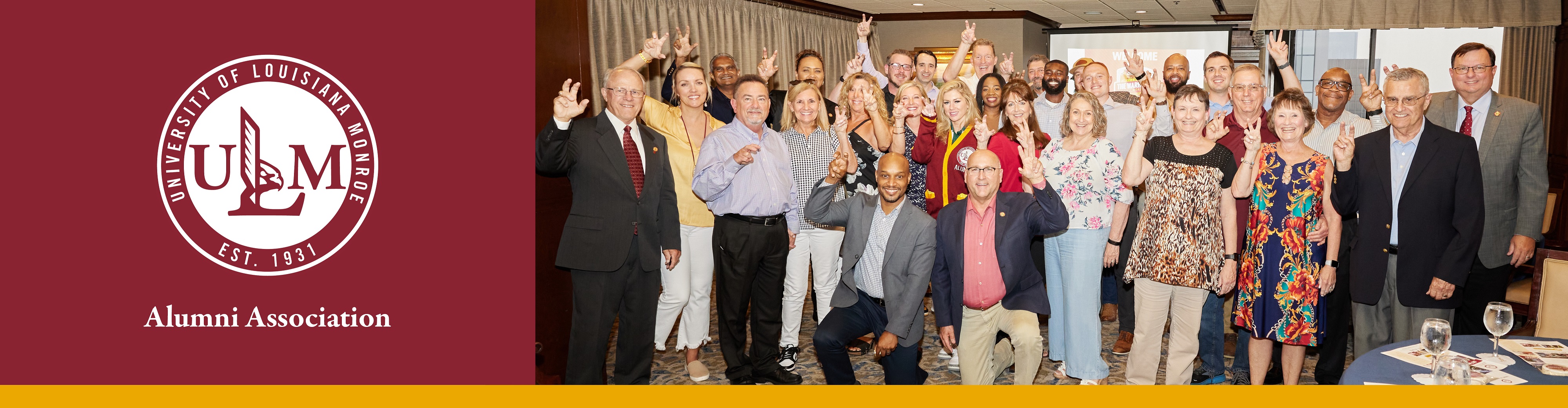 A group of people of all ages in business casual clothes smile at the camera and make the "Talons Out!" hand signal.