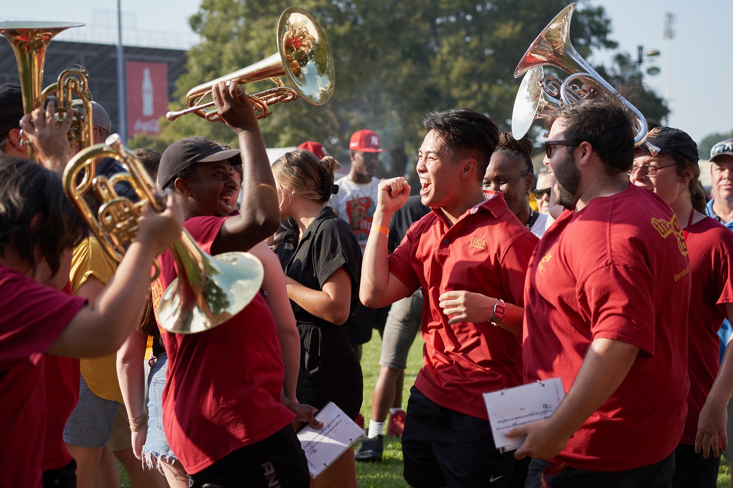 A group of students wearing maroon t-shirts cheer and hold instruments.