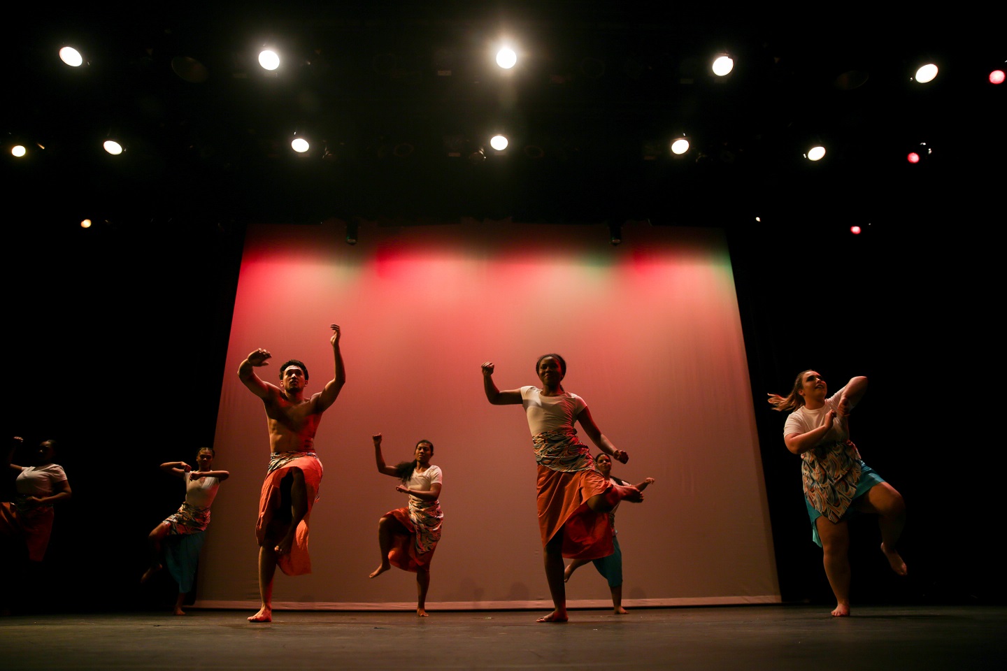 A group of people dance on a stage lit in red light.