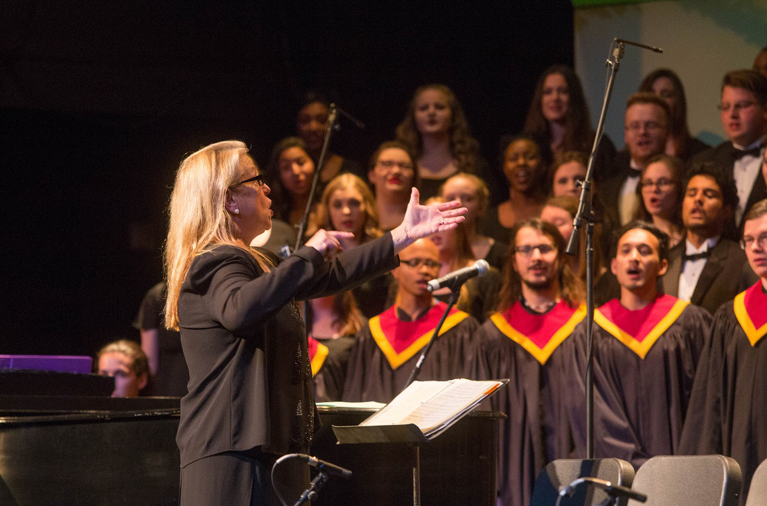 A woman directs a choir wearing black robes.