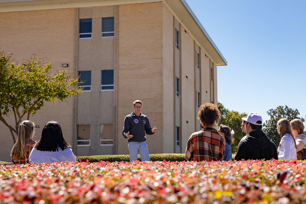 A Hawkseeker tour guide stands in front of a group of students on a ULM campus tour.
