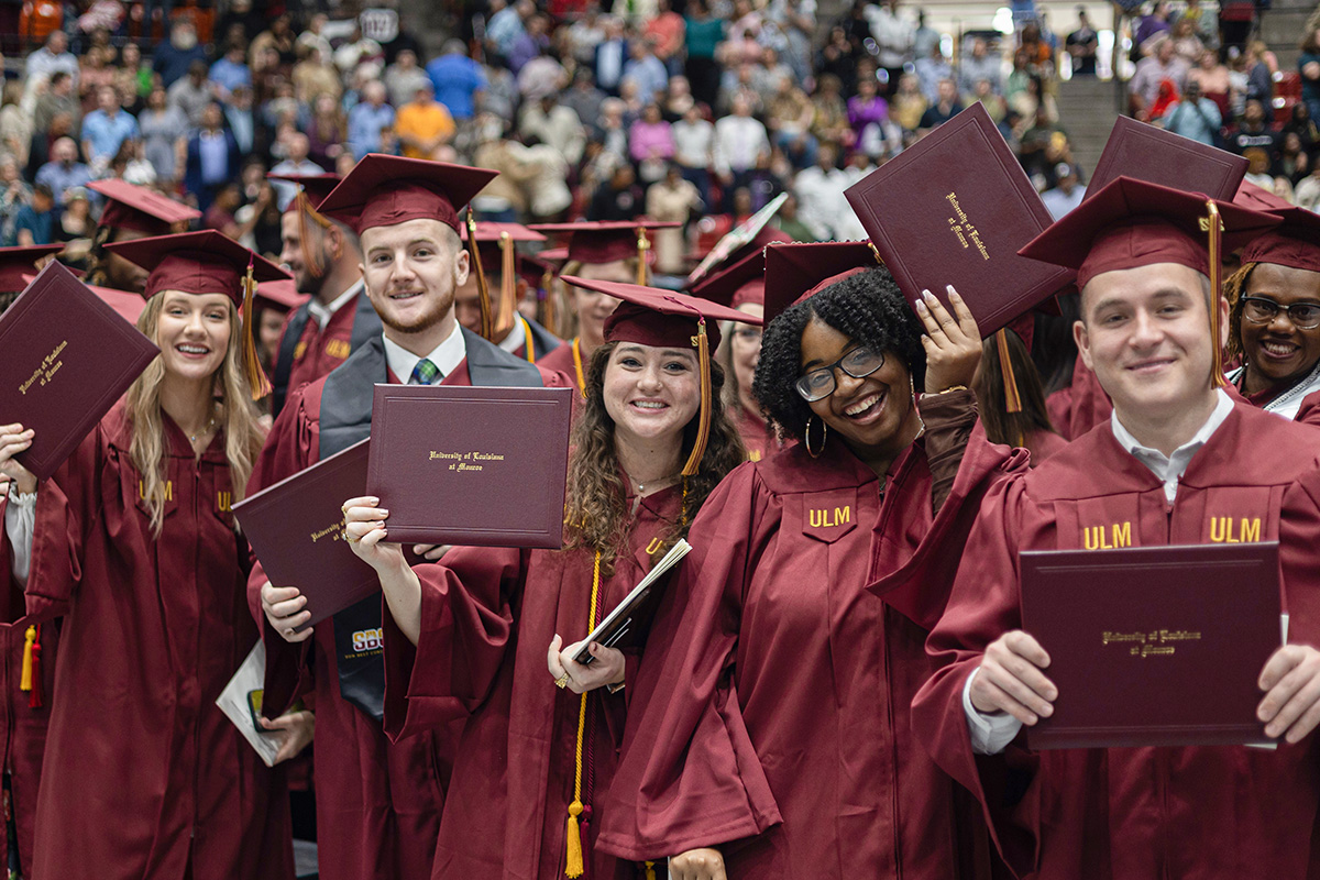 Graduates in maroon caps and gowns hold diplomas.