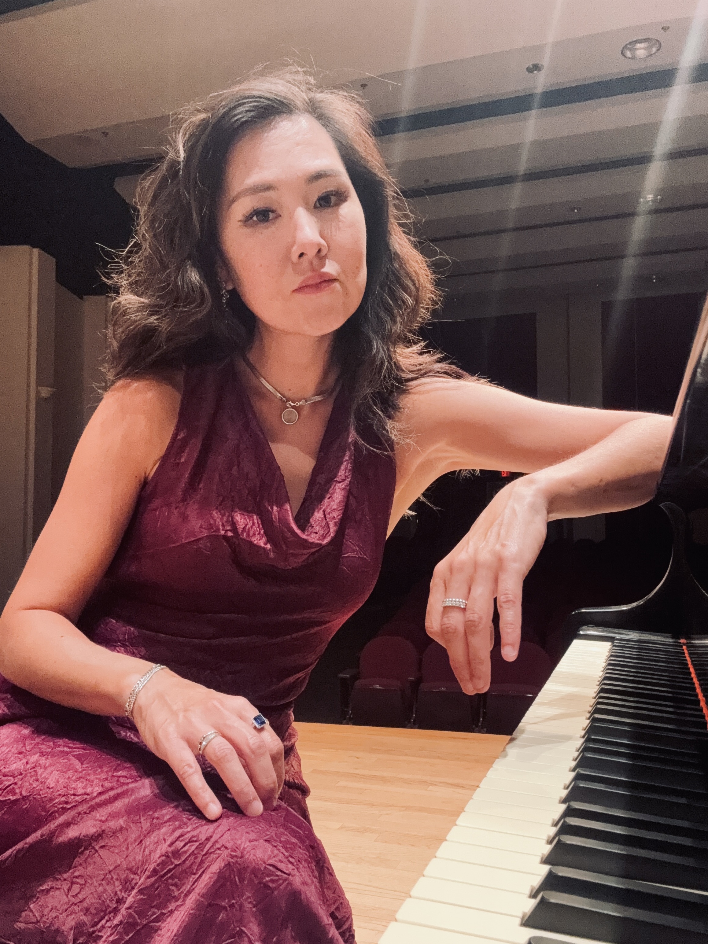 Dr. Diana Thacher is seated at a grand piano in Biedenharn Recital Hall. 