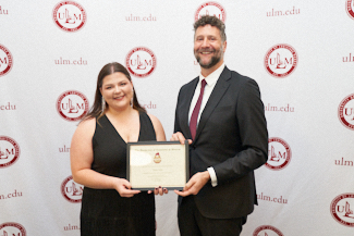 Dr. Joshua Stockley and Caitlyn Cullen smile at the camera. They hold an award.