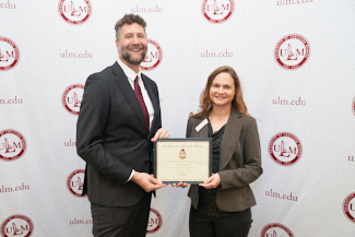 Dr. Joshua Stockley and Dr. Megan Broadway smile at the camera. They hold an award.