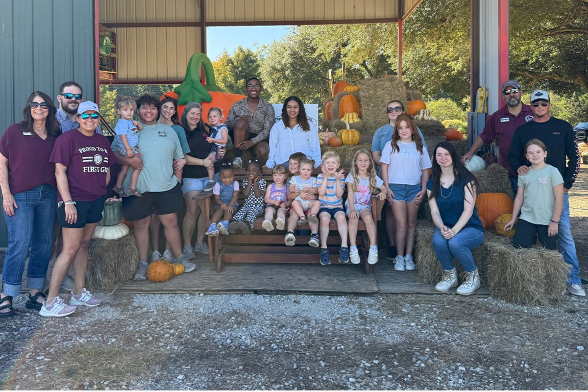 A group of people pose and smile at a pumpkin patch.