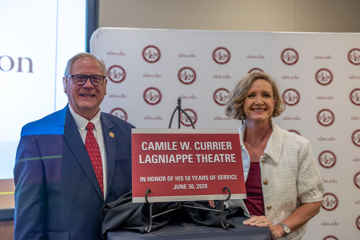 Two people stand beside a plaque that reads "Camile W. Currier Lagniappe Theatre In Honor of 50 years of service June 30, 2020"