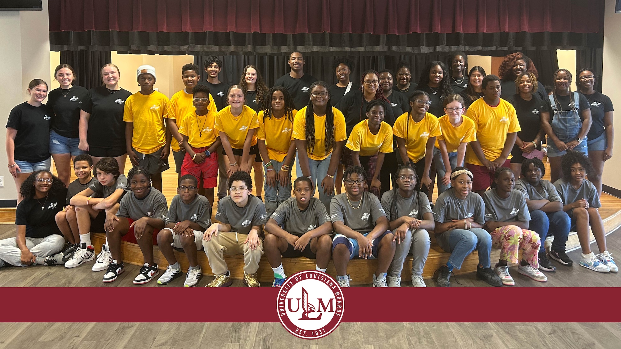 A large group of college students and middle school students stand in rows and smile. The ULM logo is displayed at the bottom of the image. 