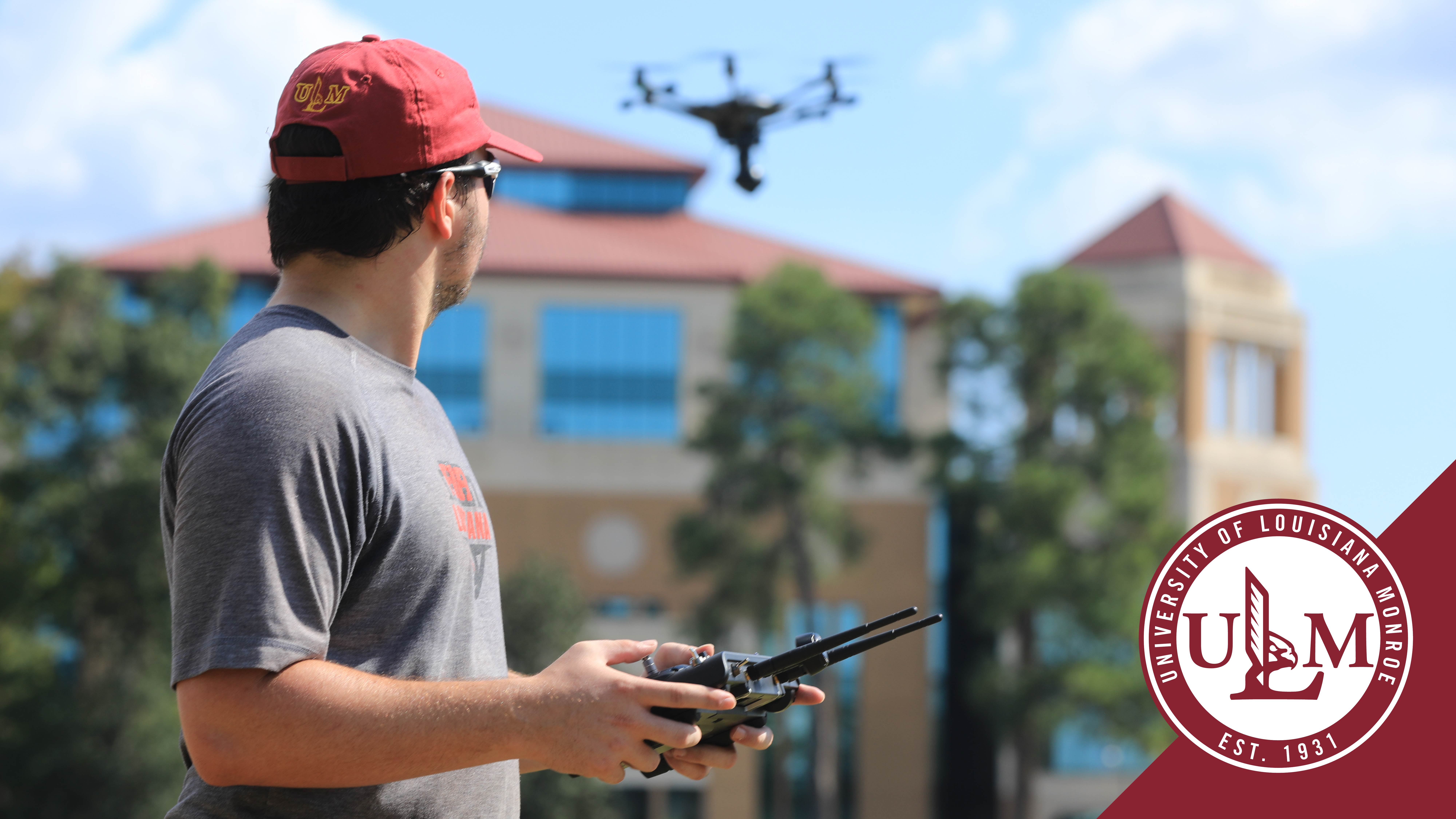 Man flies drone with ULM library in background and ULM logo in lower right corner. 