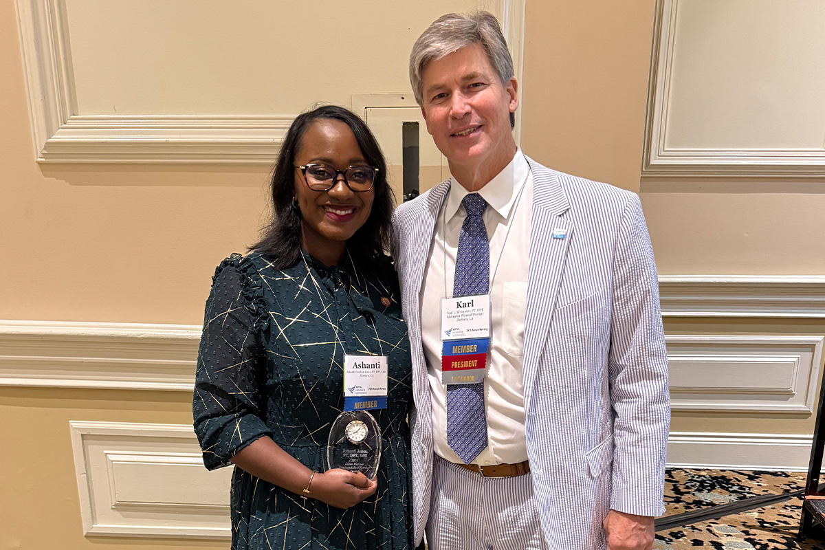 Two people standing side by side smiling. The lady on the left is holding an award. 