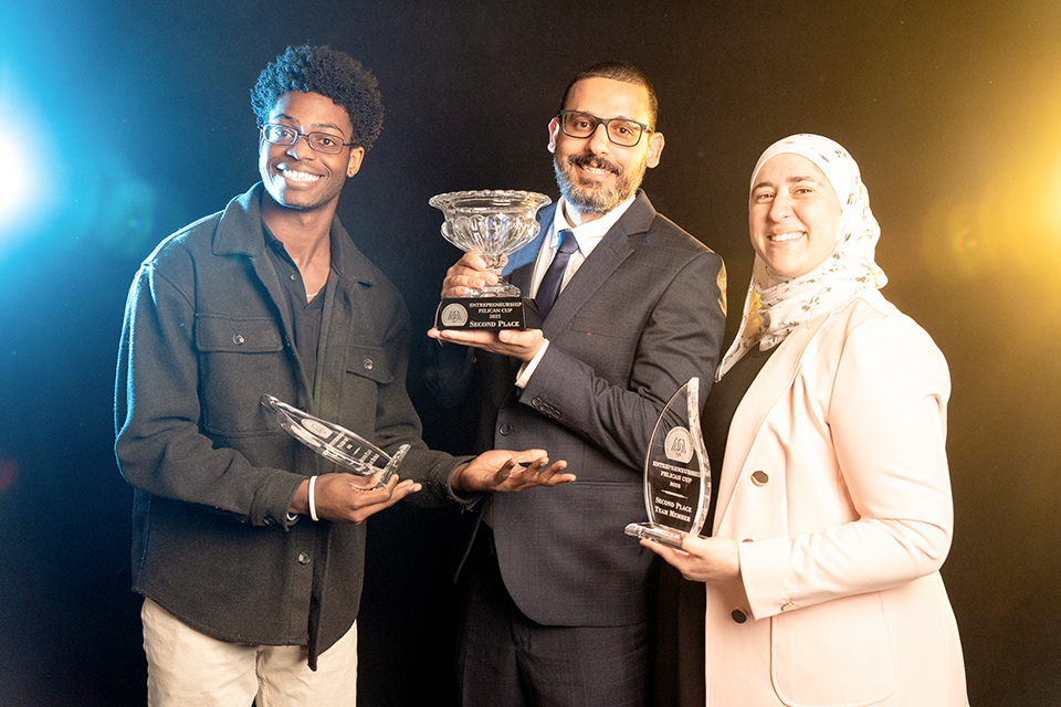 UDOIT - Pelican Cup Second Place 2025 Three people are holding trophies, with one man holding a large trophy and two smaller ones. They are all smiling and posing for a picture.