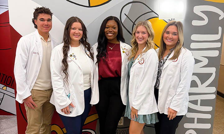 ULM COP Pharmacy Council Officers standing in front of a maroon and gold wall mural.