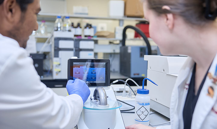 Graduate student explaining the ThermoScientific NanoDrop One to a pharmacy student.